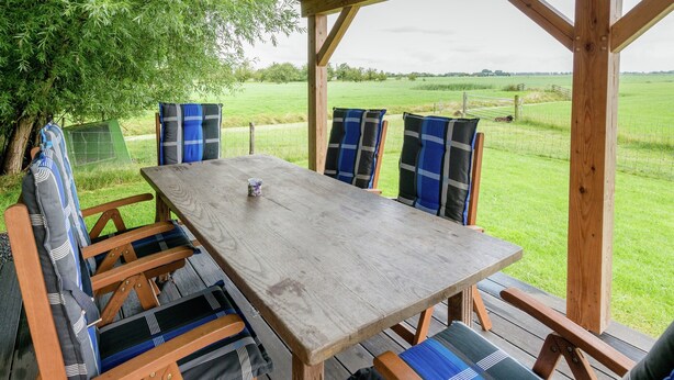 An outdoor wooden deck with a table and chairs, surrounded by a wire fence and a grassy field. - Lively Cottage near Lake in Schellinkhout (Schellinkhout)