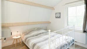 A bedroom with a bed, wooden floor, a window, and a radiator. - Lively Cottage near Lake in Schellinkhout (Schellinkhout)