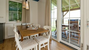 A dining area with a wooden table, white chairs, a radio, and a window with curtains. - Lively Cottage near Lake in Schellinkhout (Schellinkhout)
