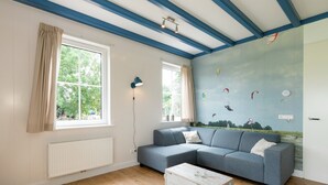 A room with a blue and white color scheme, a sectional sofa, a white coffee table, and a mural of kites on the wall. - Lively Cottage near Lake in Schellinkhout (Schellinkhout)