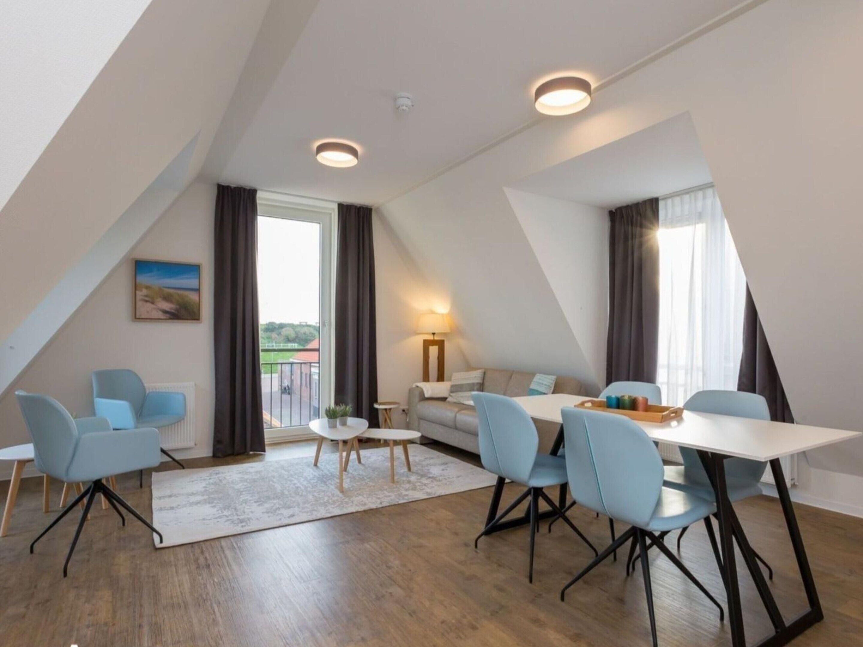 A modern loft-style room with a dining area, seating, and a view through a large window.