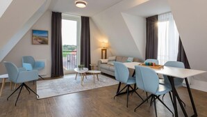 A modern loft-style room with a dining area, seating, and a view through a large window. - Alluring Apartment in Zoutelande near Center & Sea (Zoutelande)