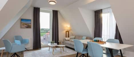 A modern loft-style room with a dining area, seating, and a view through a large window.