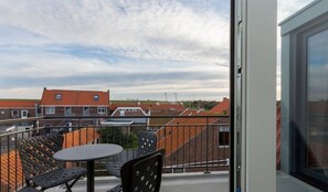 A balcony with a table and chairs, a view of neighboring houses, and a clear sky.