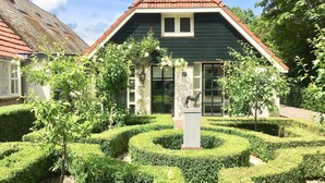 A building with a green facade and a red roof, surrounded by a well-manicured garden with hedges and trees. - Boutique Holiday Home in Nieuwleusen near Forest (Nieuwleusen)
