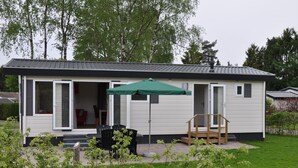 Une maison mobile de plain-pied dotée d’un patio, d’un parasol vert et d’une petite terrasse en bois.