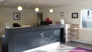 Un comptoir d’accueil avec un logo, une horloge et une fenêtre avec des stores.