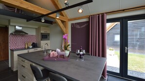 A modern kitchen with a central island, wooden beams, and a view to the outside. - Holiday Home in Alphen-chaam With Terrace (Alphen)