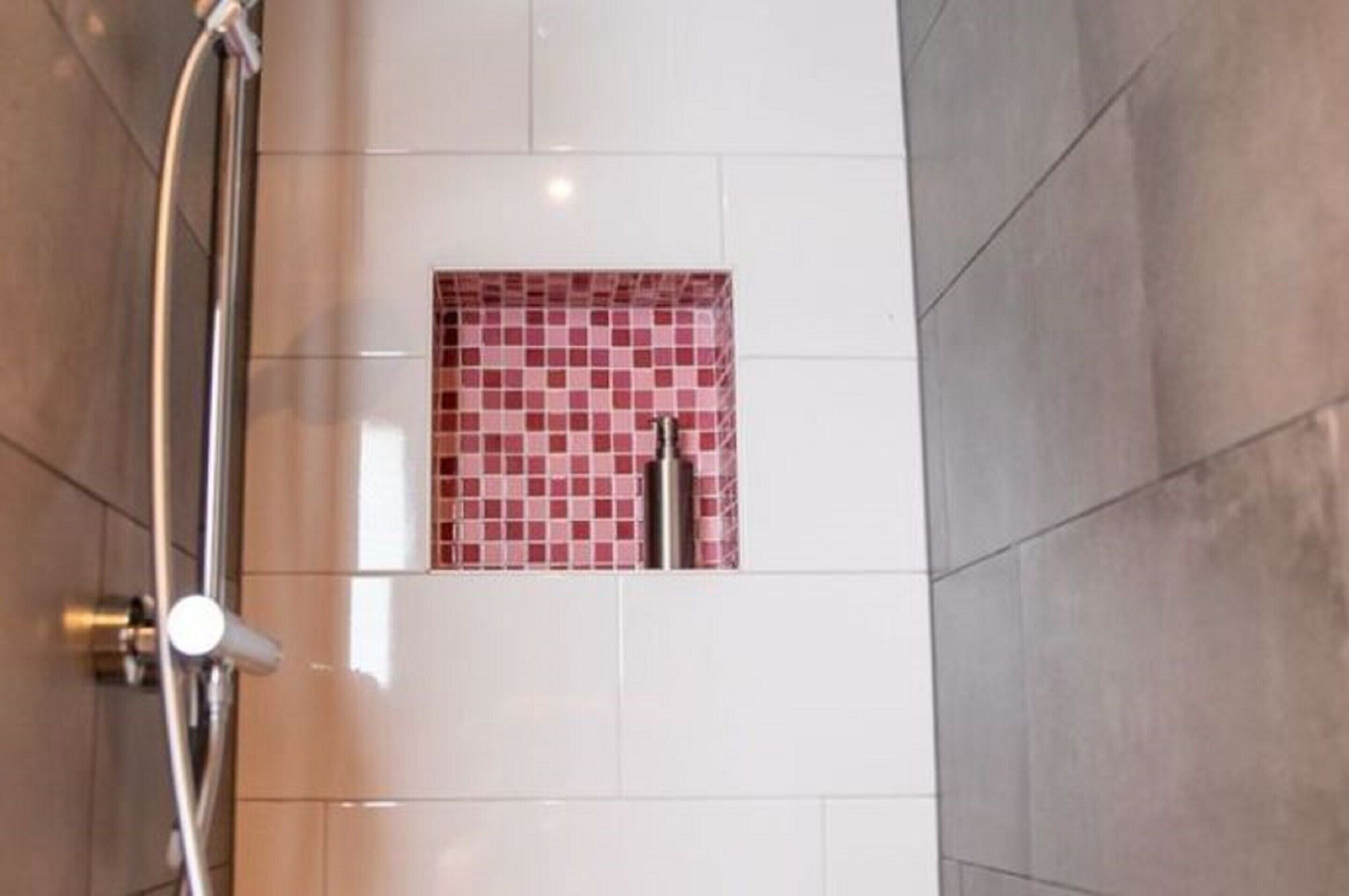 A bathroom with a shower area, a tiled wall with a pink mosaic pattern, and a white tiled floor.