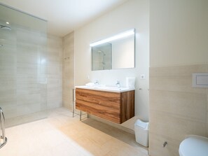 Un bagno moderno con doccia in vetro, un mobile contenitore in legno e uno specchio grande.