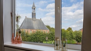 A window with a view of a church and a garden. - Holiday Home in Koudekerke Near Seabeach (Koudekerke)