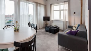 A modern living room with a round dining table, a grey sofa, and a TV. - Holiday Home in Koudekerke Near Seabeach (Koudekerke)