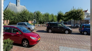A parking area with several cars, a church with a clock tower, and a bus in the background. - Holiday Home in Koudekerke Near Seabeach (Koudekerke)