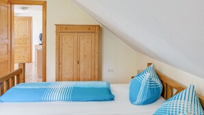 Un dormitorio con techo inclinado, armario de madera y cama con ropa de cama a rayas azules y blancas.