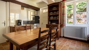 A dining area with a wooden table and chairs, a kitchen with appliances, and a window with curtains. - Quaint Holiday Home With Garden (Payzac)
