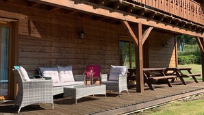 A wooden cabin with a balcony featuring tree silhouettes, wicker furniture, and a picnic table. - Chalet in Ventron Near La Bresse Ski Area (Ventron)