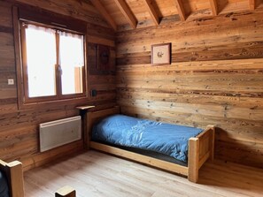 A small, wooden cabin-style room with a single bed, a window with curtains, and a radiator. - Chalet in Ventron Near La Bresse Ski Area (Ventron)