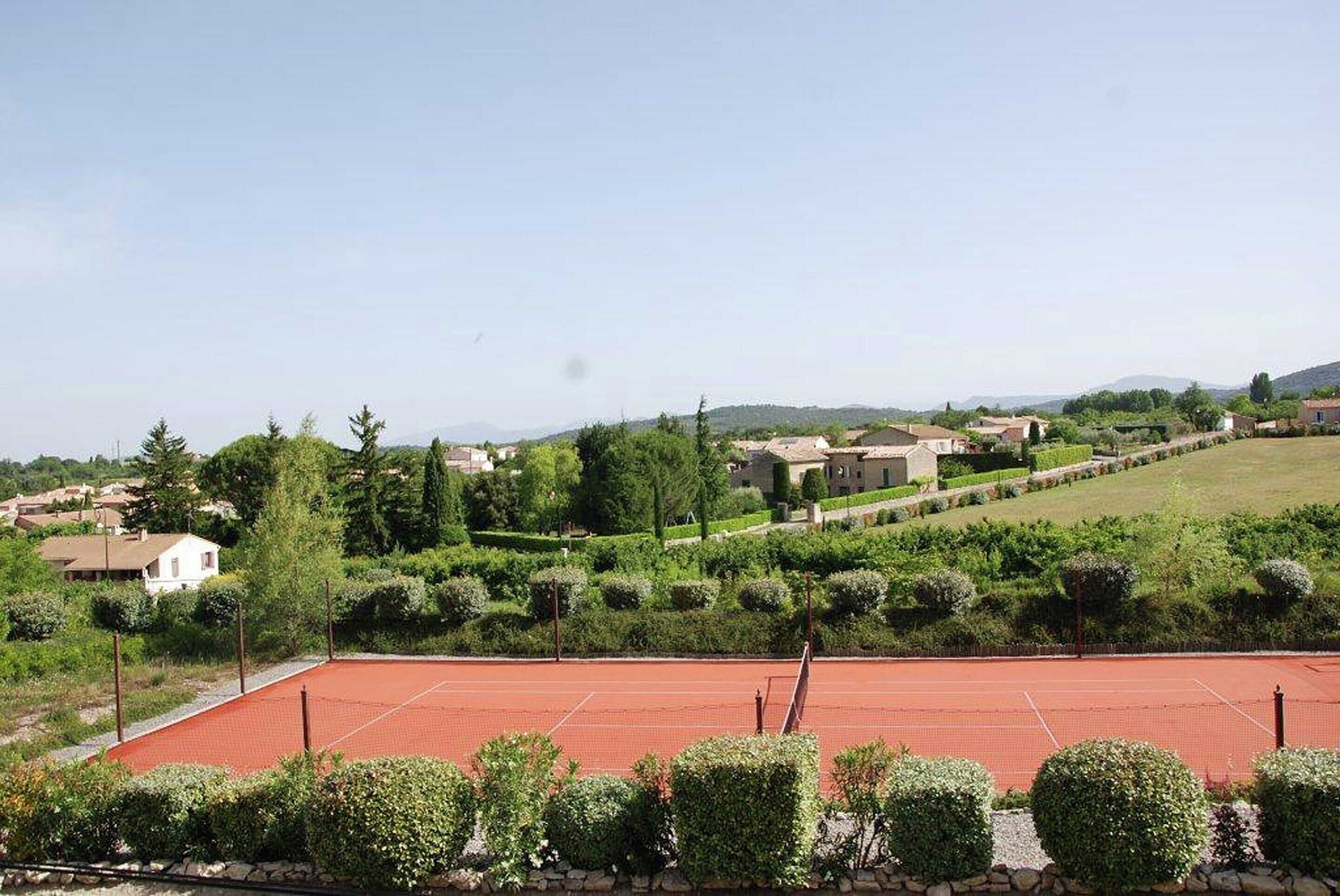 A tennis court surrounded by greenery and houses in a hilly area.