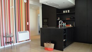 A modern kitchen with a central island, black cabinetry, and a colorful striped wall. - Villa in Malaucene With Private Pool (Malaucene)