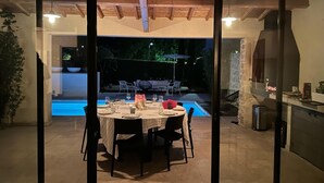 An indoor dining area with a view of an outdoor swimming pool, a stone fireplace, and a grill. - Villa in Malaucene With Private Pool (Malaucene)