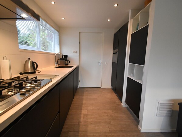 A modern kitchen with a gas stove, sink, and a window with blinds. - Bungalow Near Veerse Meer With Private Garden (Kamperland)
