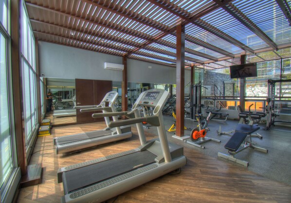 Academia com esteiras, aparelhos de musculação e um espelho grande.
