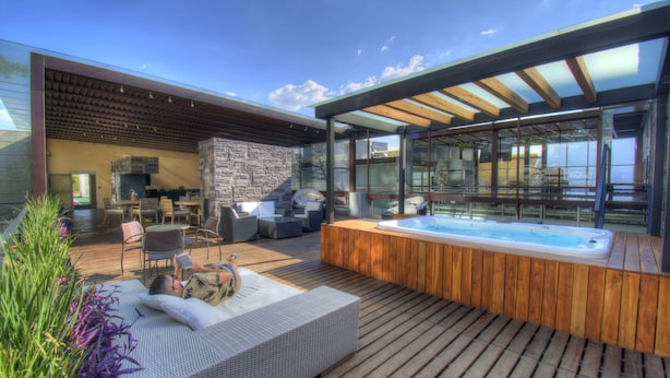 Une terrasse extérieure moderne dotée d’un jacuzzi, d’un espace salon et d’un mur en pierre.