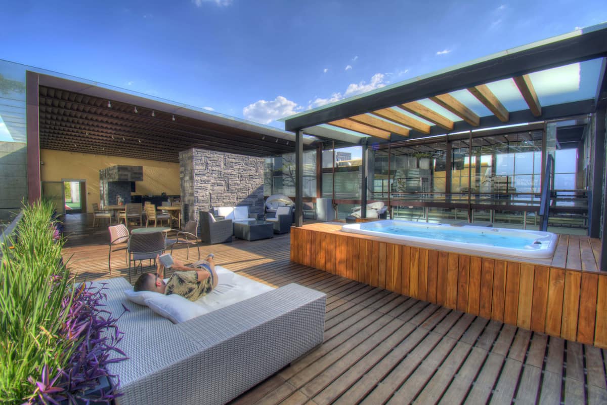 A modern outdoor deck with a hot tub, seating area, and a stone wall.