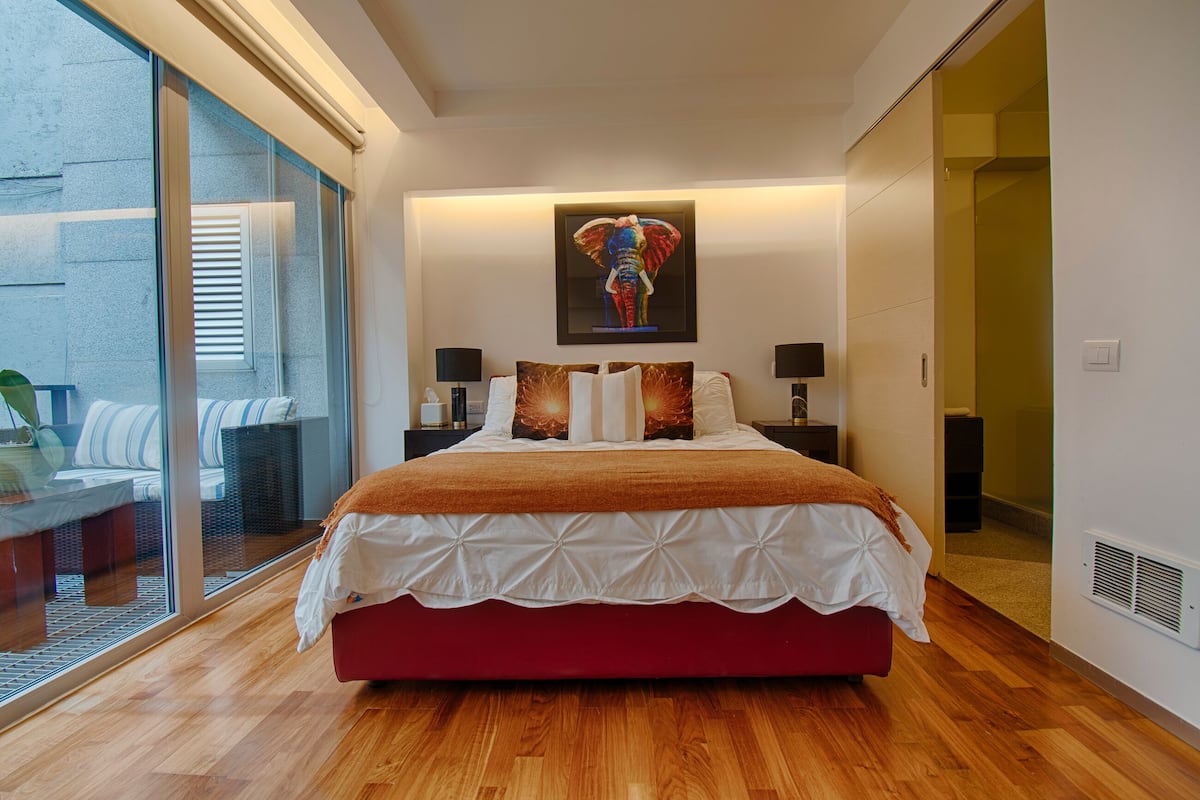 A modern bedroom with a large bed, a glass wall, and a framed artwork above the bed.