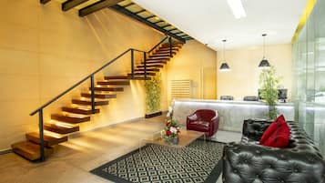 Un hall d’entrée moderne avec un escalier, un comptoir d’accueil, un canapé en cuir et un tapis à motifs.