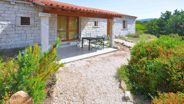 A stone house with a red-tiled roof, a covered patio with a table and chairs, and a gravel pathway leading to the entrance. - Residence a Badesi ID 3348 (Badesi)