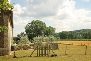 Uma propriedade rural com um edifício de tijolos, um jardim cercado e um campo ao fundo.
