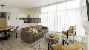 Ein modernes Wohnzimmer mit einer Couch, Sesseln, einem Couchtisch und einem Essbereich mit Tisch und Stühlen.