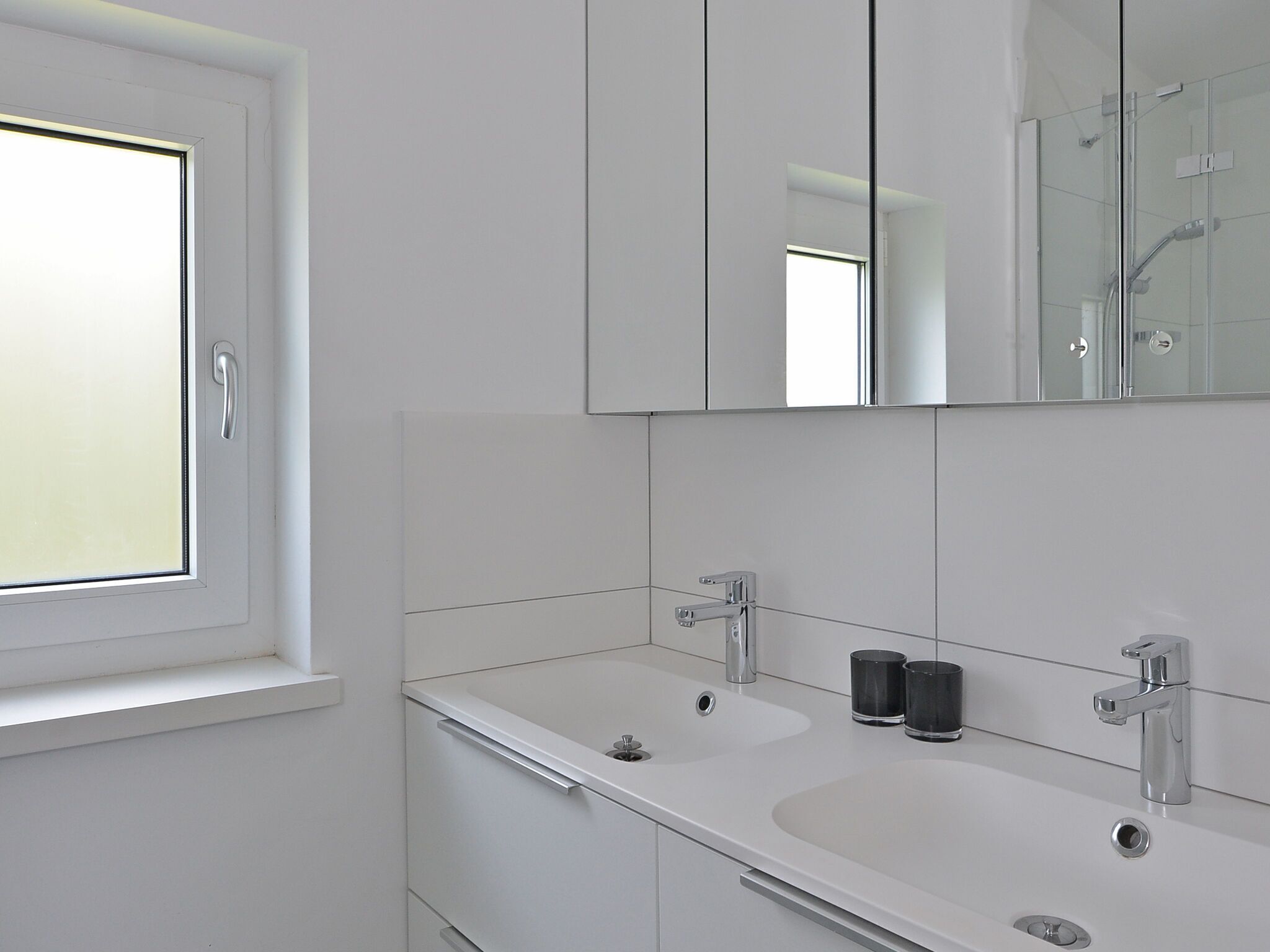 Une salle de bain moderne avec un grand miroir, deux lavabos et une fenêtre.