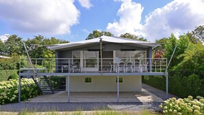 Une maison moderne à deux étages, dotée d’un balcon, d’un espace salon extérieur et d’une allée gravillonnée.