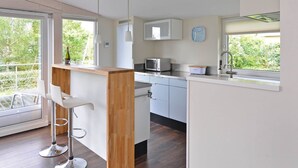 Une cuisine moderne avec des meubles blancs, un îlot central en bois et une vue sur la verdure à l’extérieur.