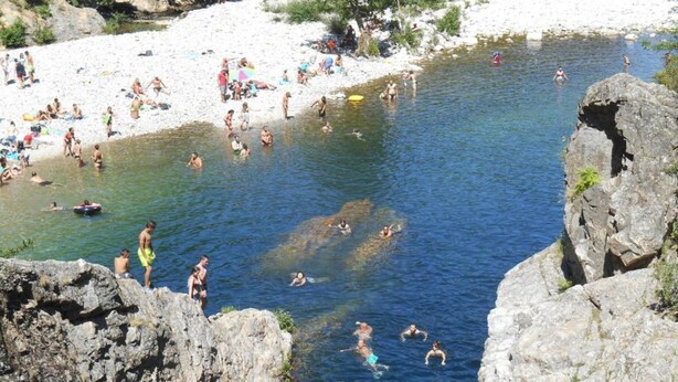 Una zona de bany natural amb formacions rocoses i una platja de sorra.
