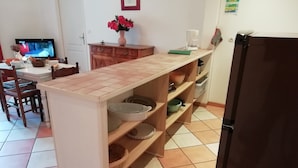 A kitchen with a wooden countertop, shelves with dishes, a refrigerator, and a TV in the background. - Quend-plage Apartment With Pool (Quend)