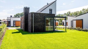 Une maison moderne dotée d’une grande porte vitrée, d’une cheminée en briques et d’une pelouse bien entretenue.