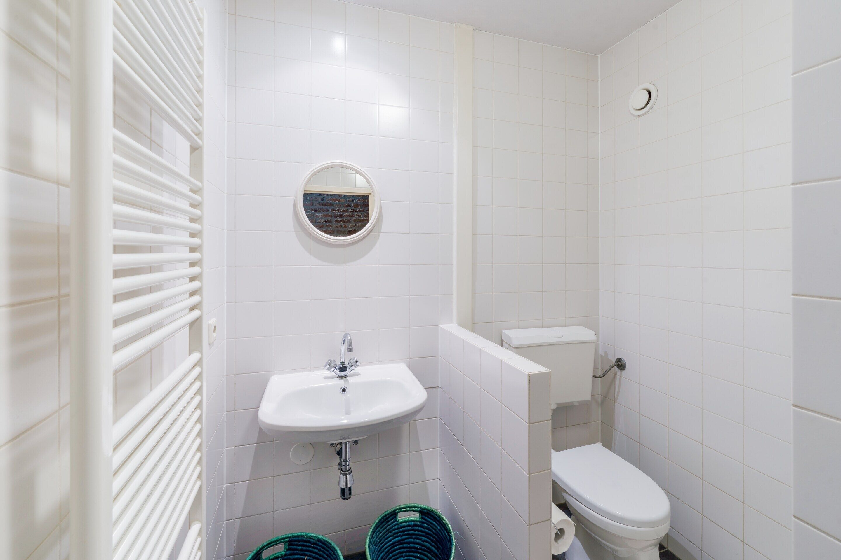 A bathroom with a white sink, toilet, and a mirror. There are two green baskets on the floor.