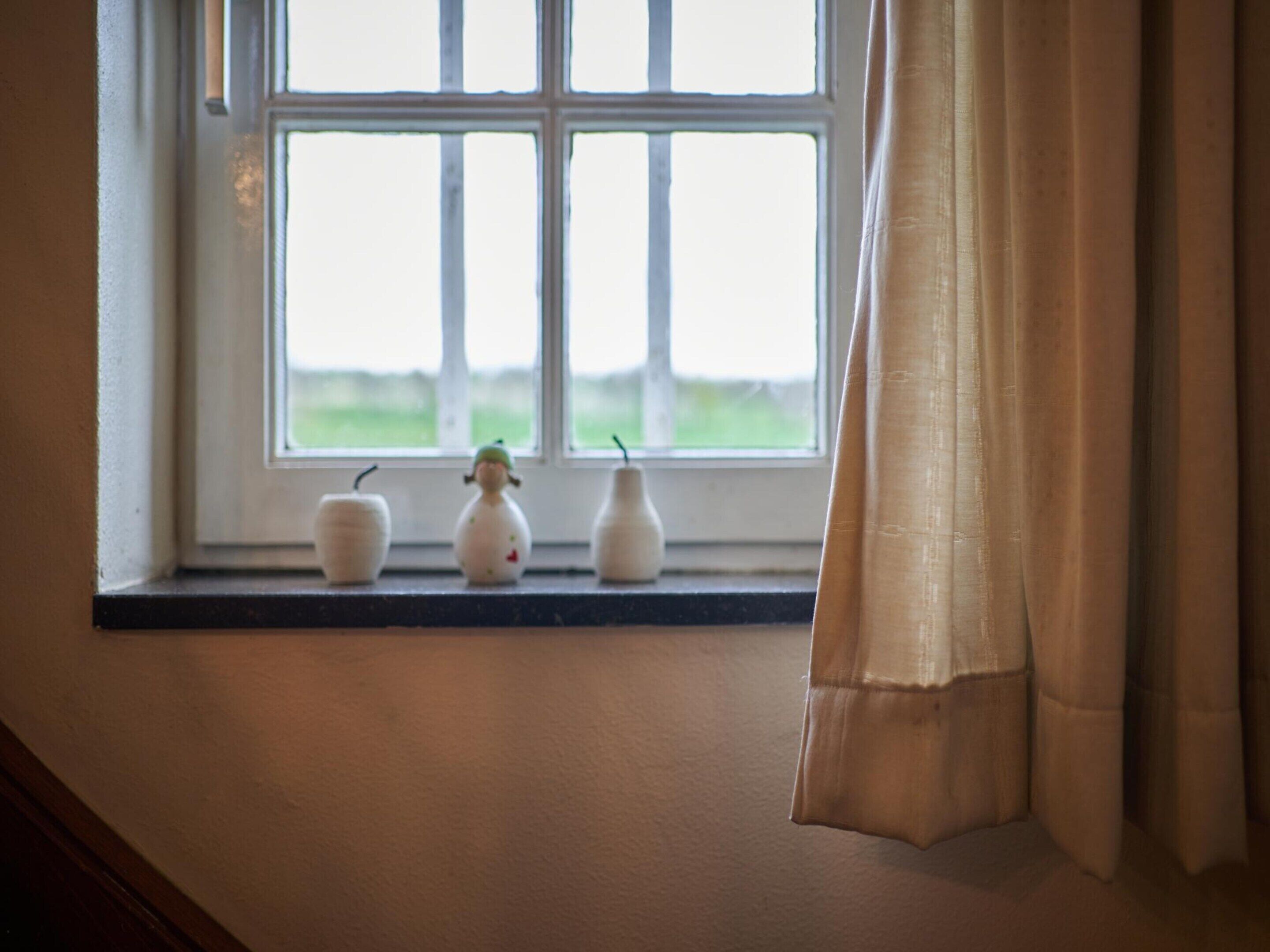 Et vindue med tre små, hvide vaser på vindueskarmen.