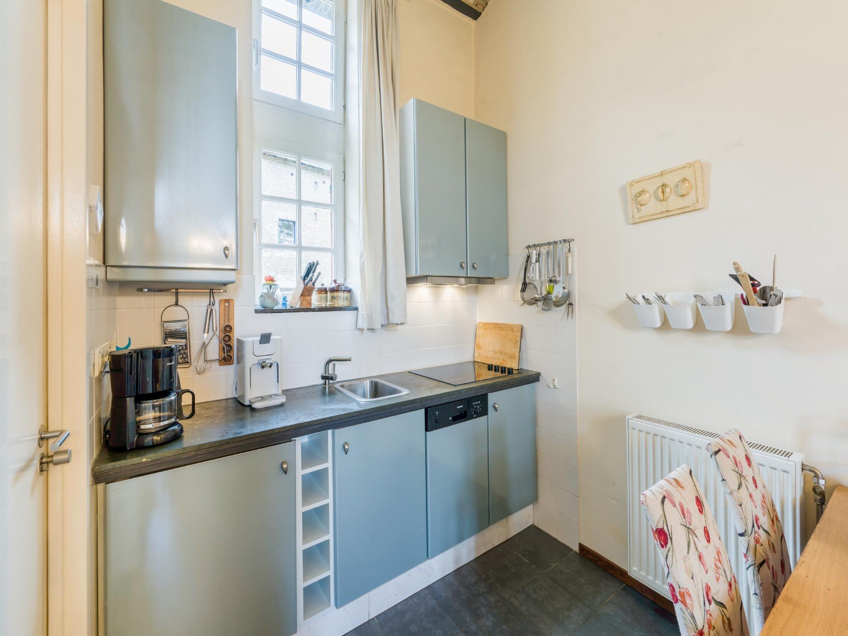 A compact kitchen with a built-in dishwasher, a coffee maker, and a window with curtains.
