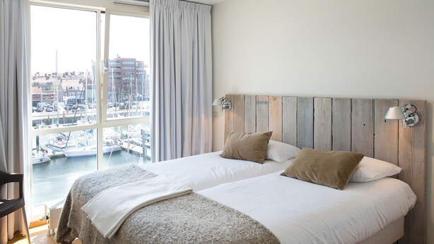A hotel room with a large bed, a view of a marina, and a wooden headboard. - Sunlit Retreat With Balcony (The Hague)
