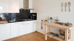 A modern kitchen with white cabinets, a black countertop, a stainless steel range hood, and a wooden table with baskets. - Sunlit Retreat With Balcony (The Hague)