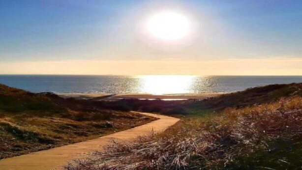 Een kustpad dat naar de zee leidt, met een heldere lucht en zon.