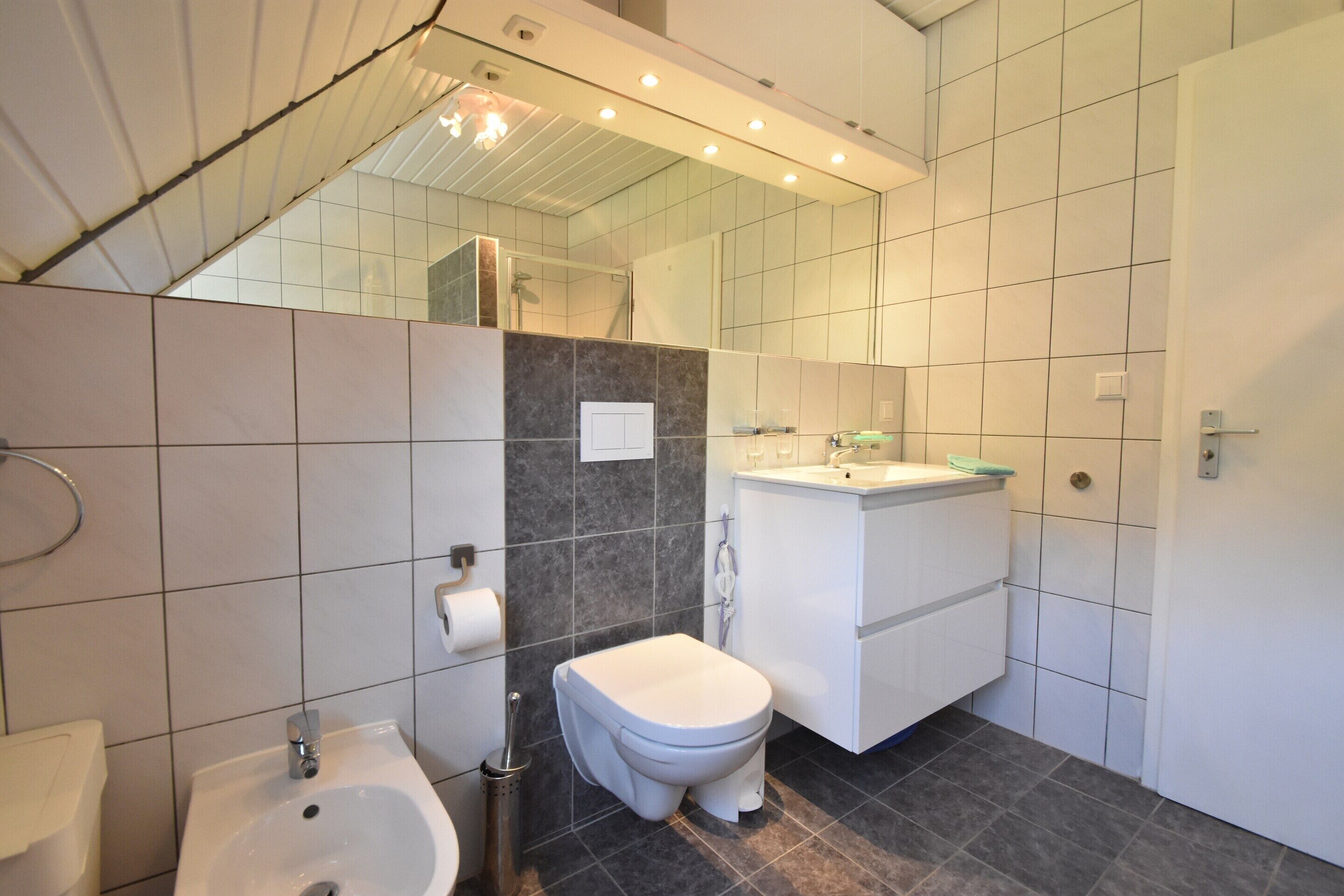 Ein modernes Badezimmer mit integriertem Bidet, Toilette, Waschbecken und Spiegel.