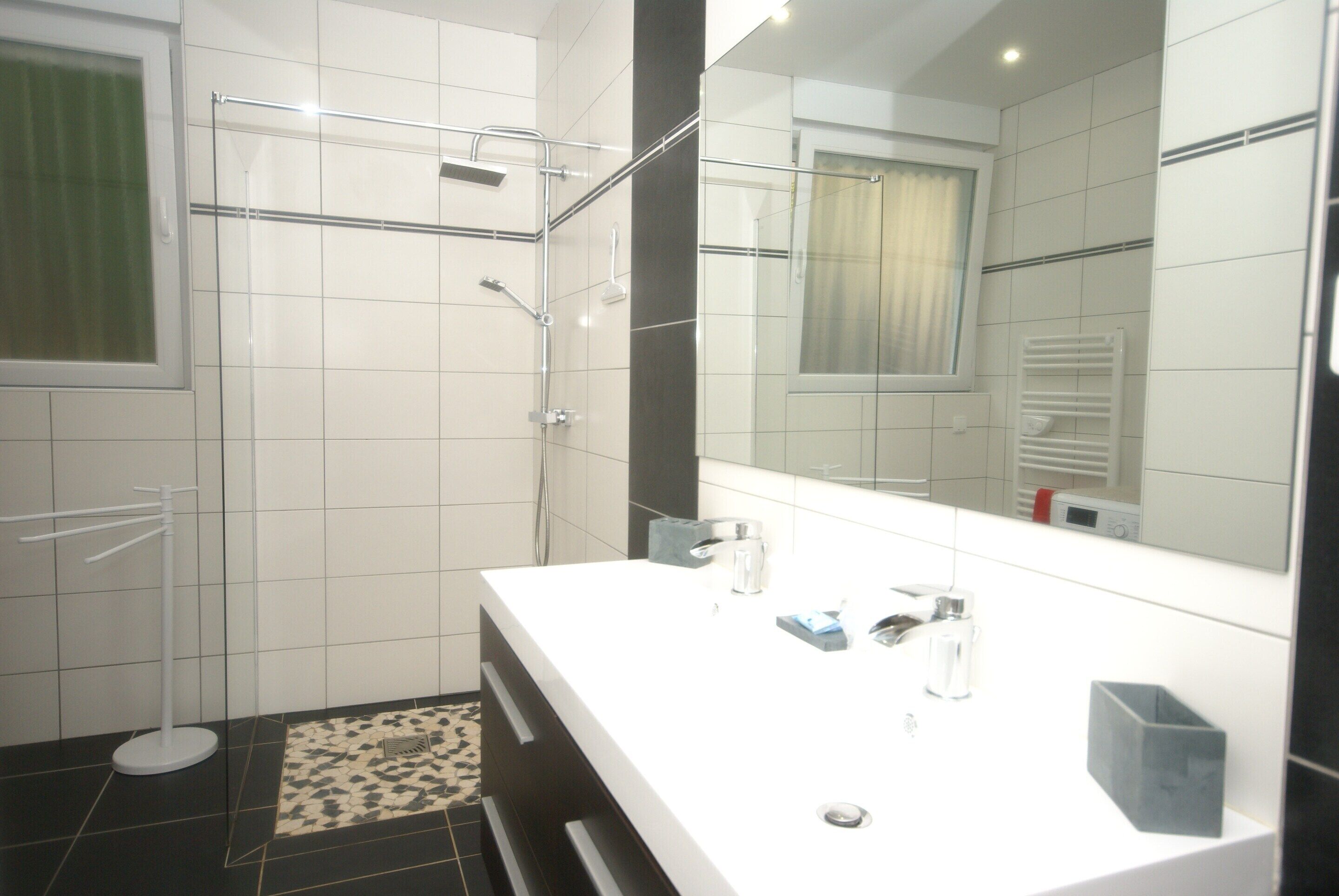 Un baño moderno con un lavamanos blanco, un espejo grande y una zona de ducha.