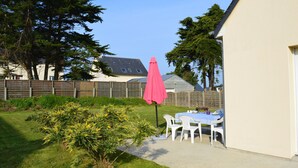 A patio area with a table and chairs, a pink umbrella, and a small garden. - Denneville Coastal Escape With Garden (Port-Bail-sur-Mer)