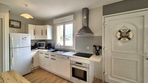 A compact kitchen with a refrigerator, microwave, stove, sink, and a large window. - Denneville Coastal Escape With Garden (Port-Bail-sur-Mer)