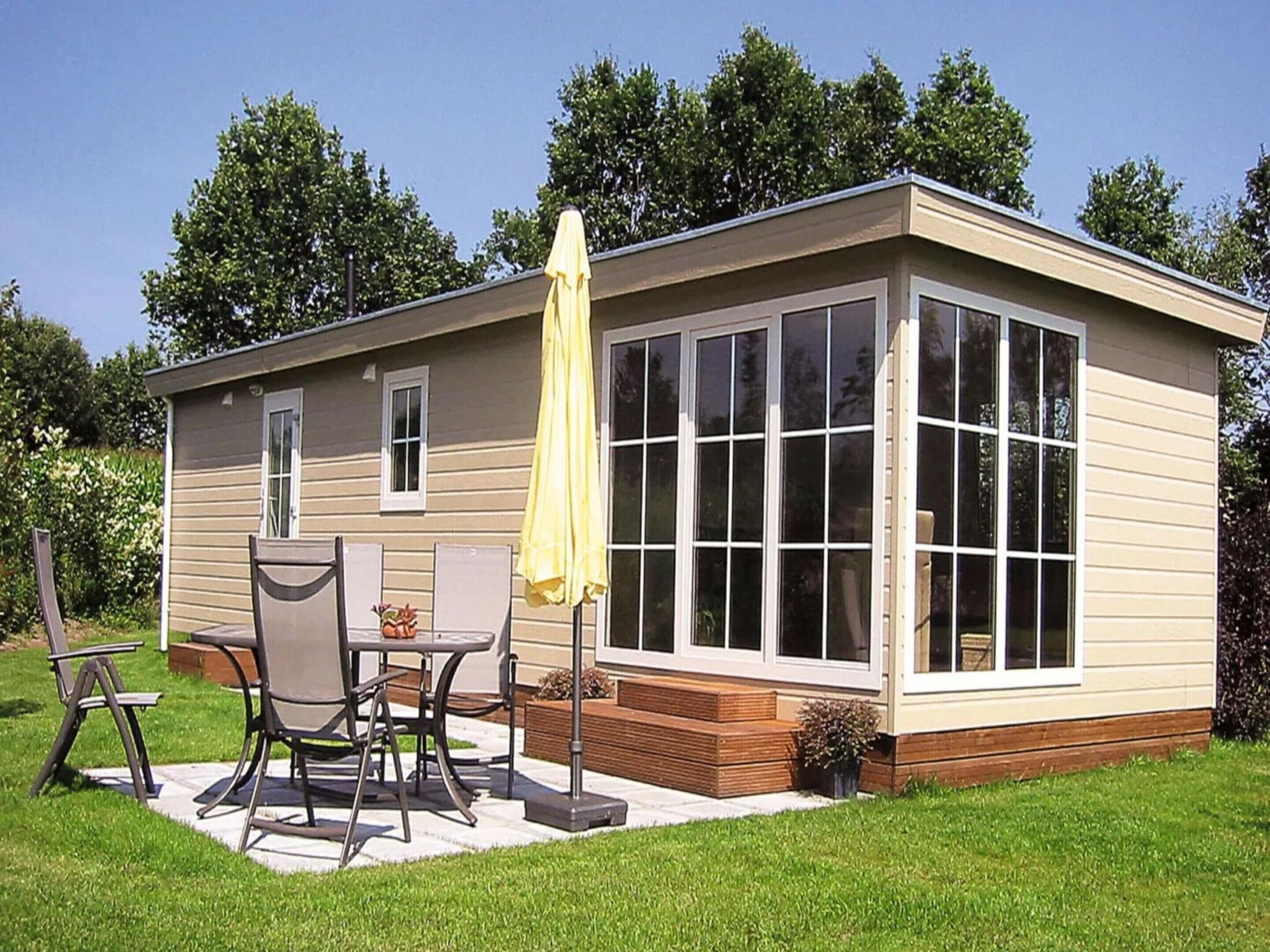 A single-story mobile home with a patio area, a table with chairs, and a yellow umbrella.